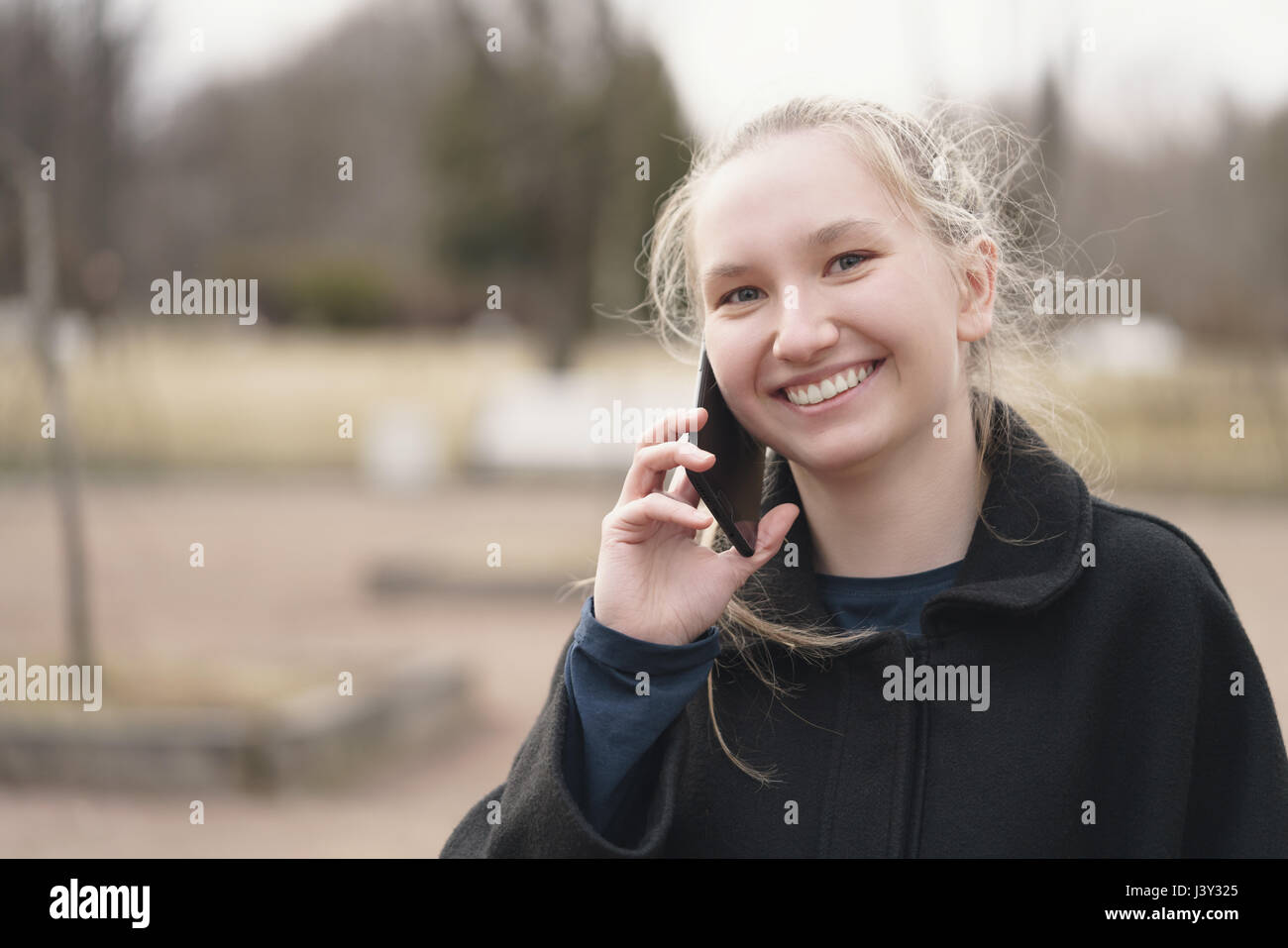 teen girl standing on sidewalk and talking on the phone early spring Stock Photo