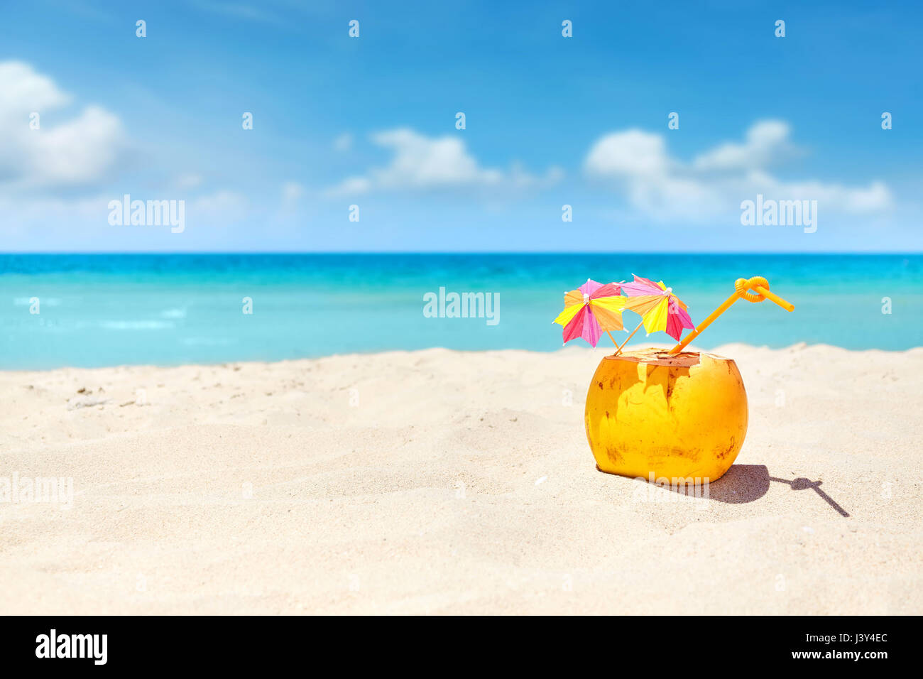 Coconut cocktail with straw and colorful umbrellas on a beach, summer holiday concept, selective focus, space for text. Stock Photo