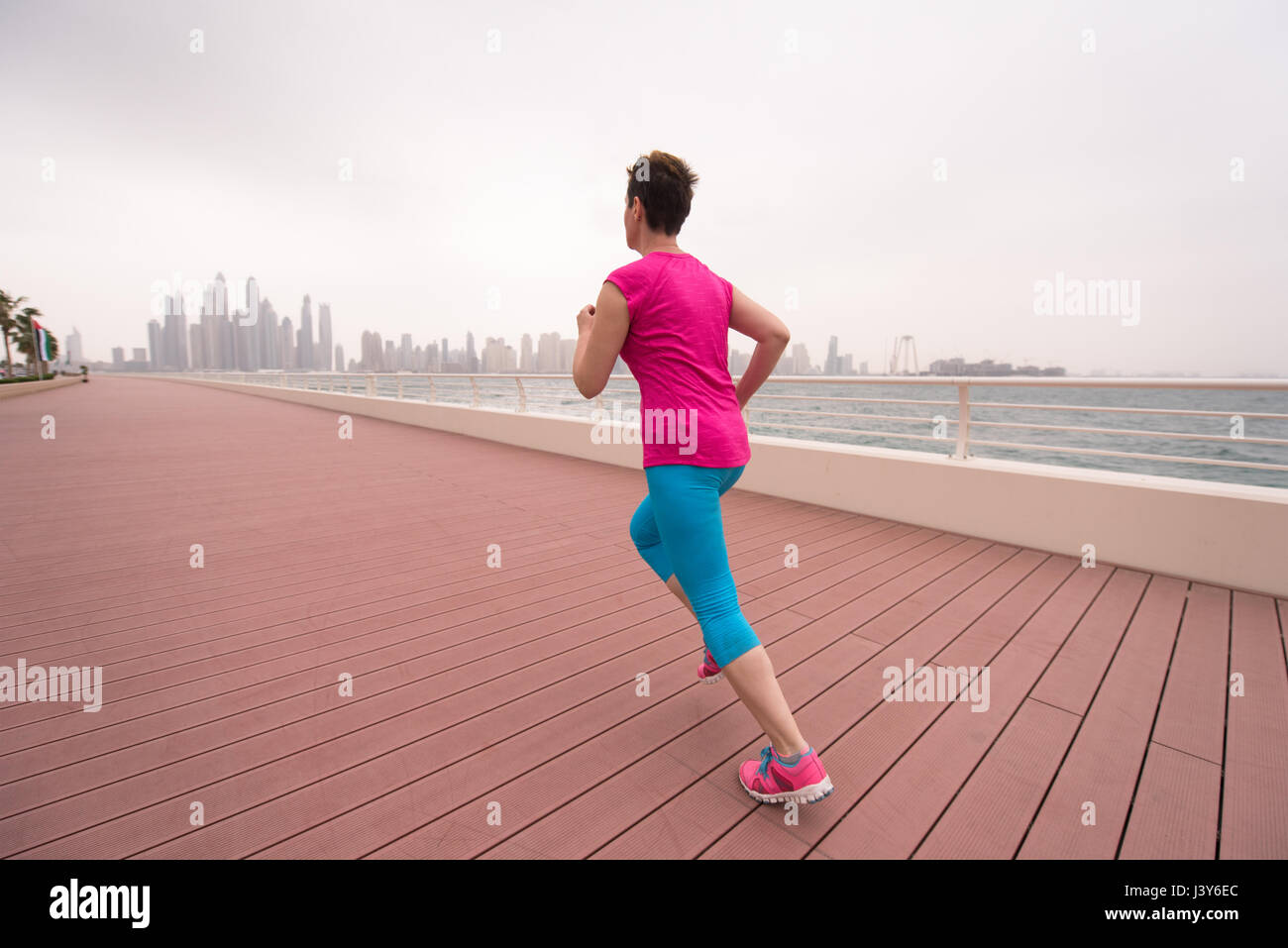 very active young beautiful woman busy running on the promenade along ...