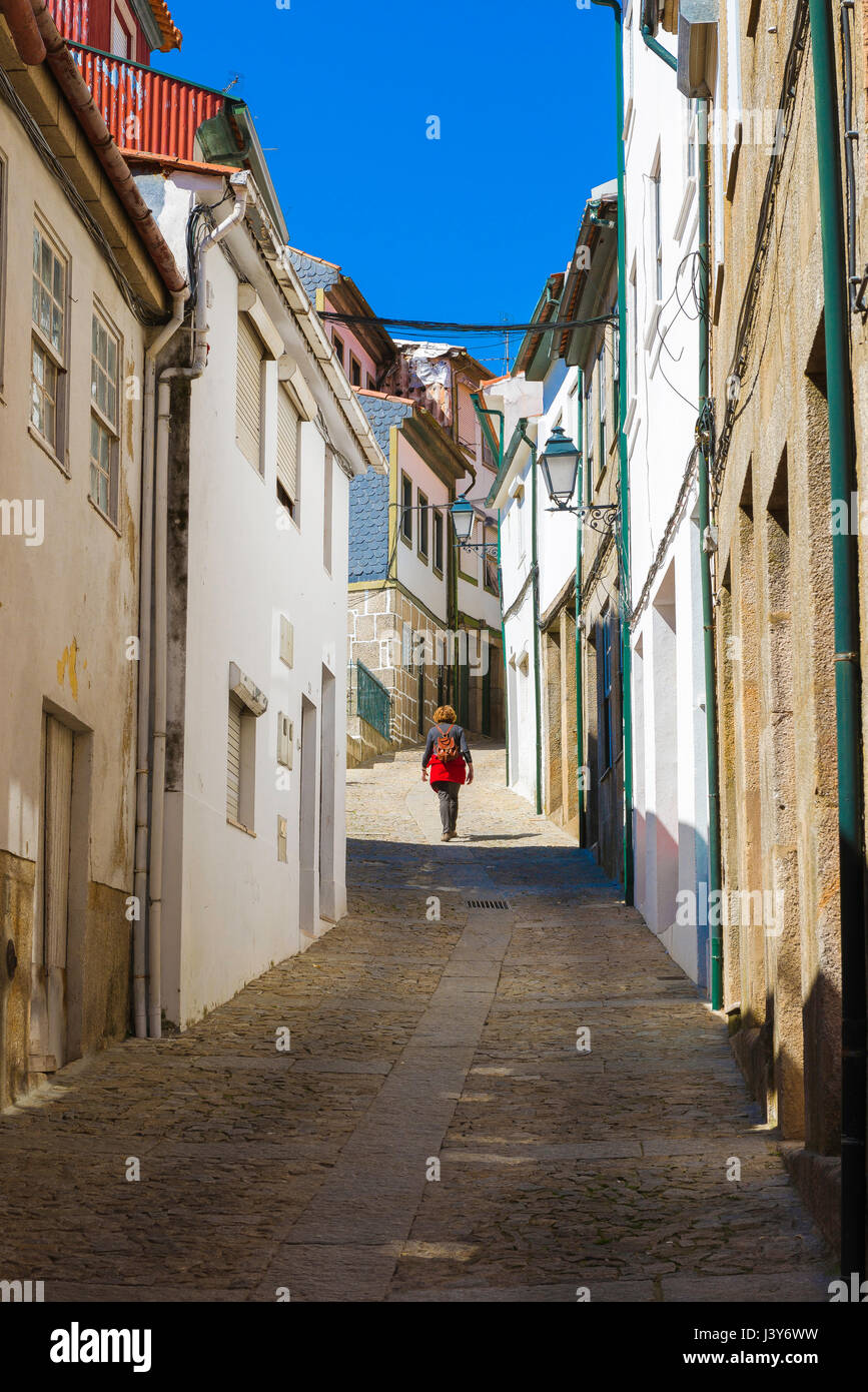 Woman walking alone concept, rear view of a solo woman traveler exploring a deserted street in the hill top town of Lamego, Portugal. Stock Photo