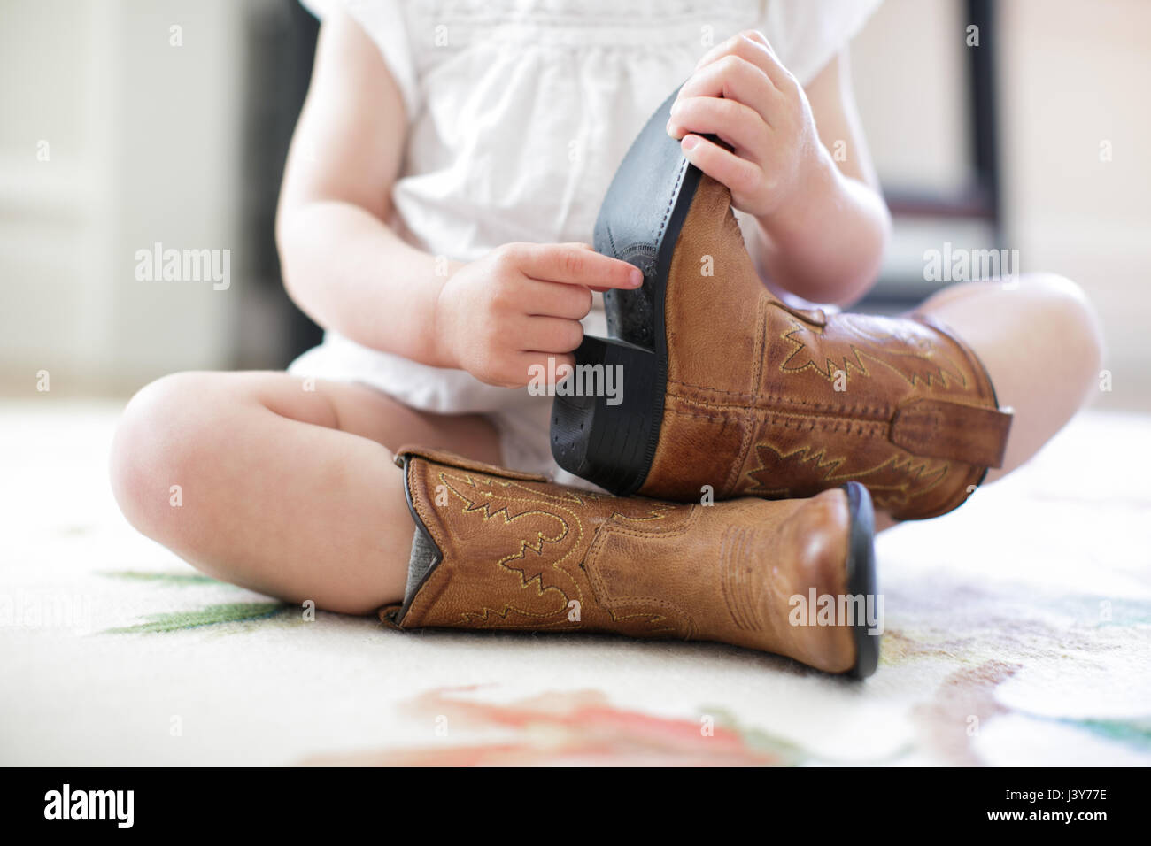 Neck down view of female toddler sitting on floor wearing cowboy boots  Stock Photo - Alamy