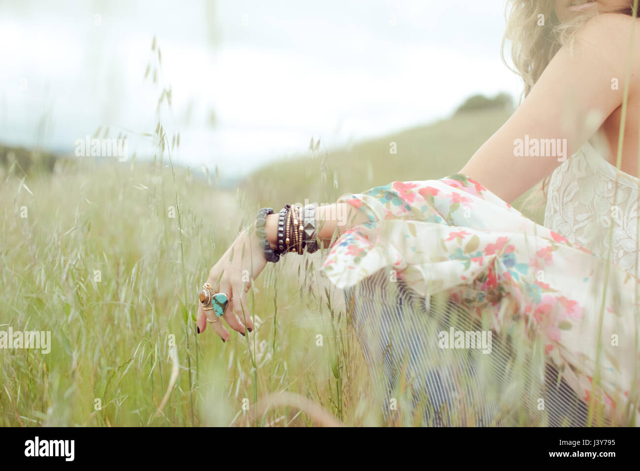 Cropped shot of boho woman wearing bangles and rings sitting in field ...