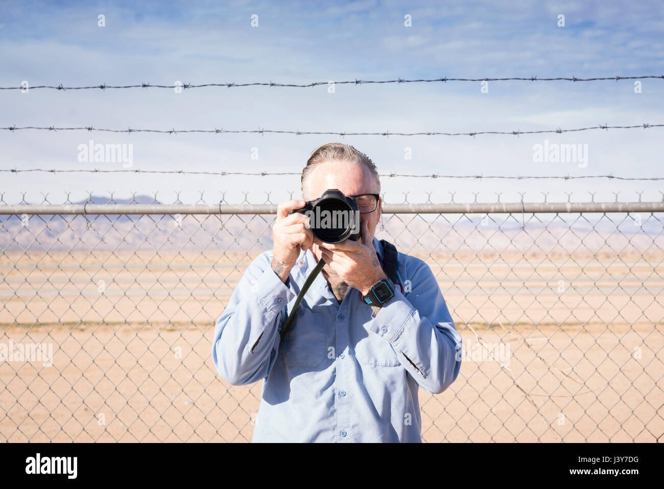 Photographer in front of barbed wire fence in desert taking photograph, California, USA Stock Photo