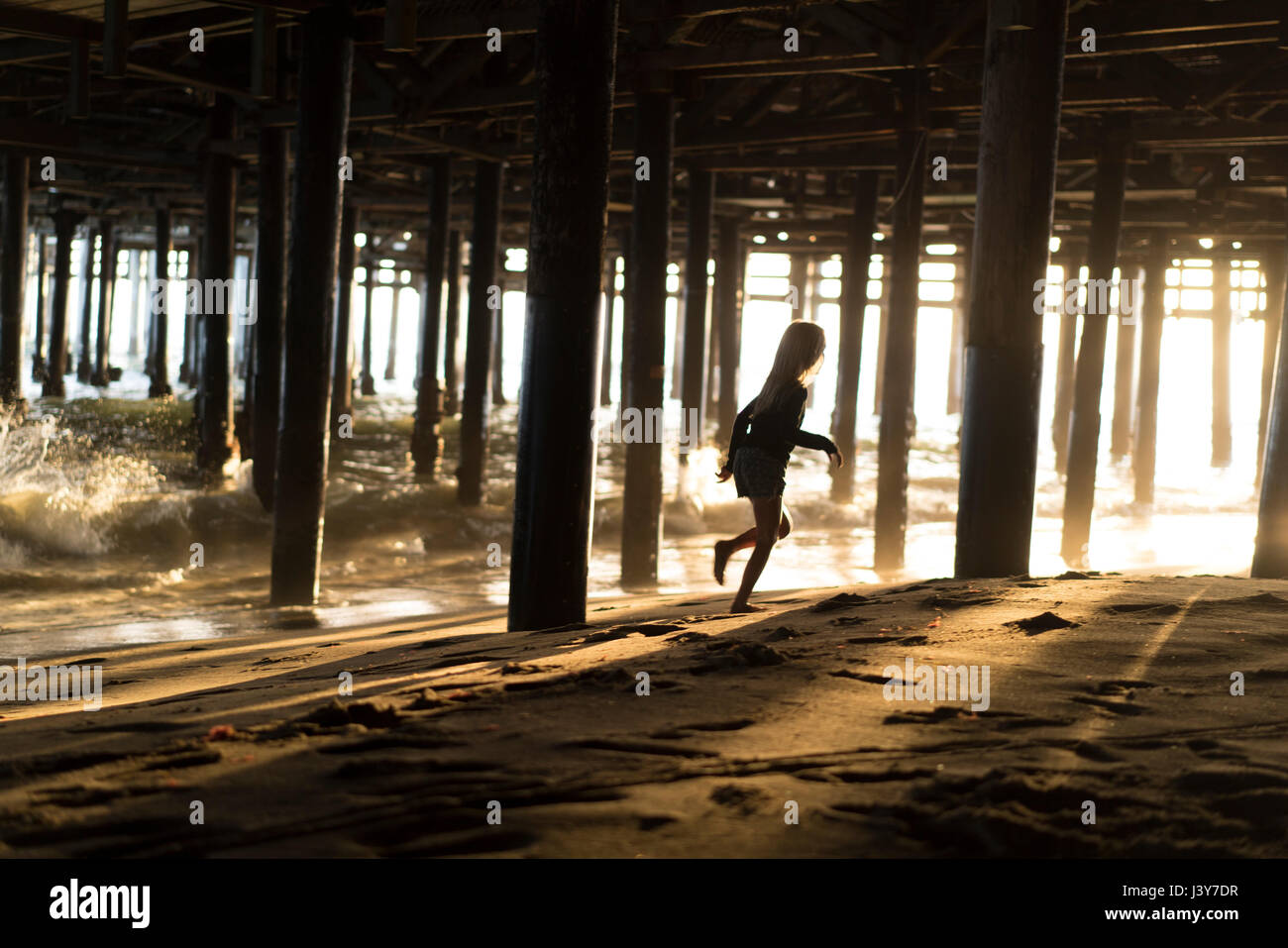 Silhouette of girl running from lapping waves underneath Santa Monica pier, California, USA Stock Photo