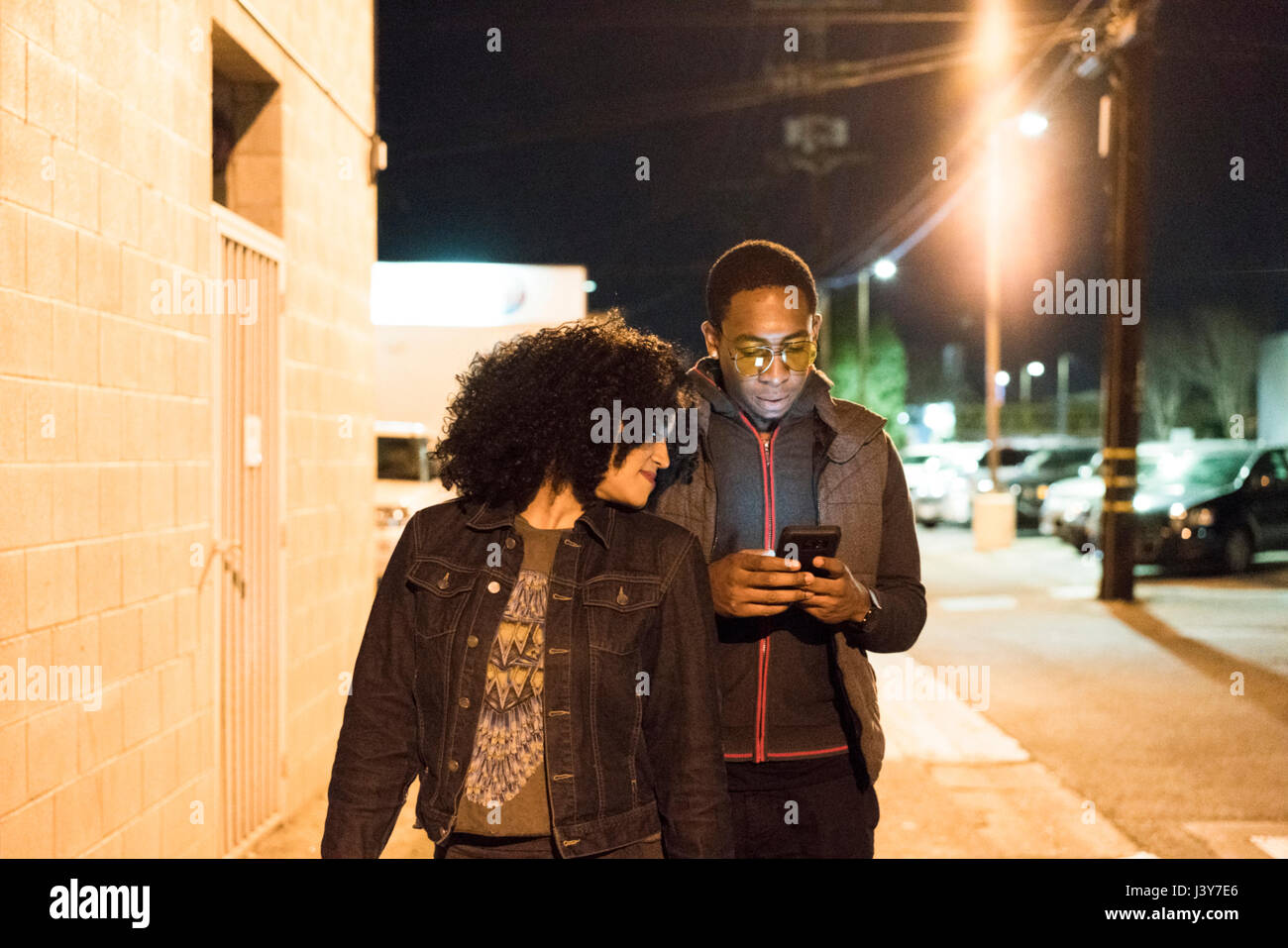 Couple walking in street at night looking at smartphone, Los Angeles, California, USA Stock Photo