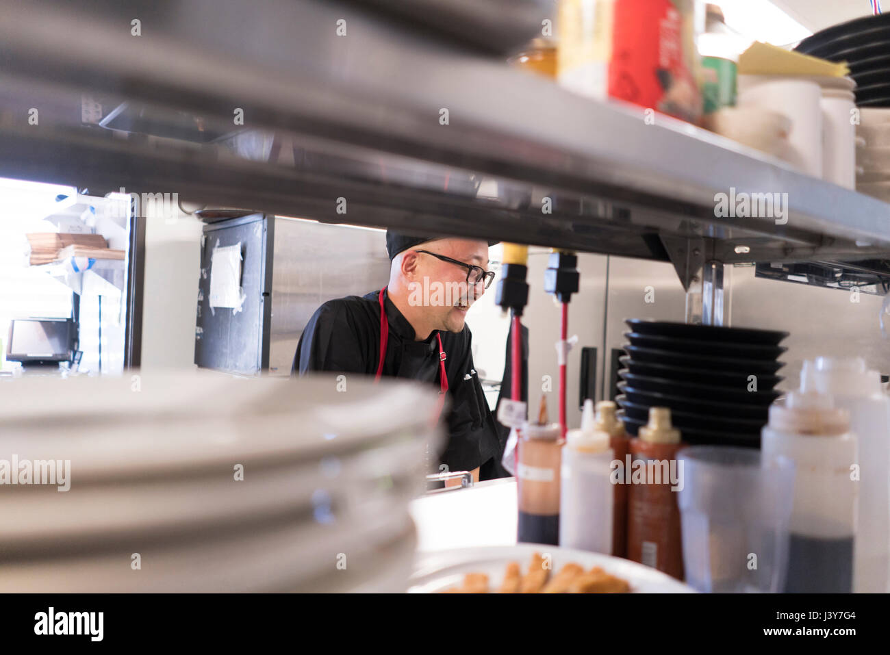 View through shelves of chef working in commercial kitchen Stock Photo