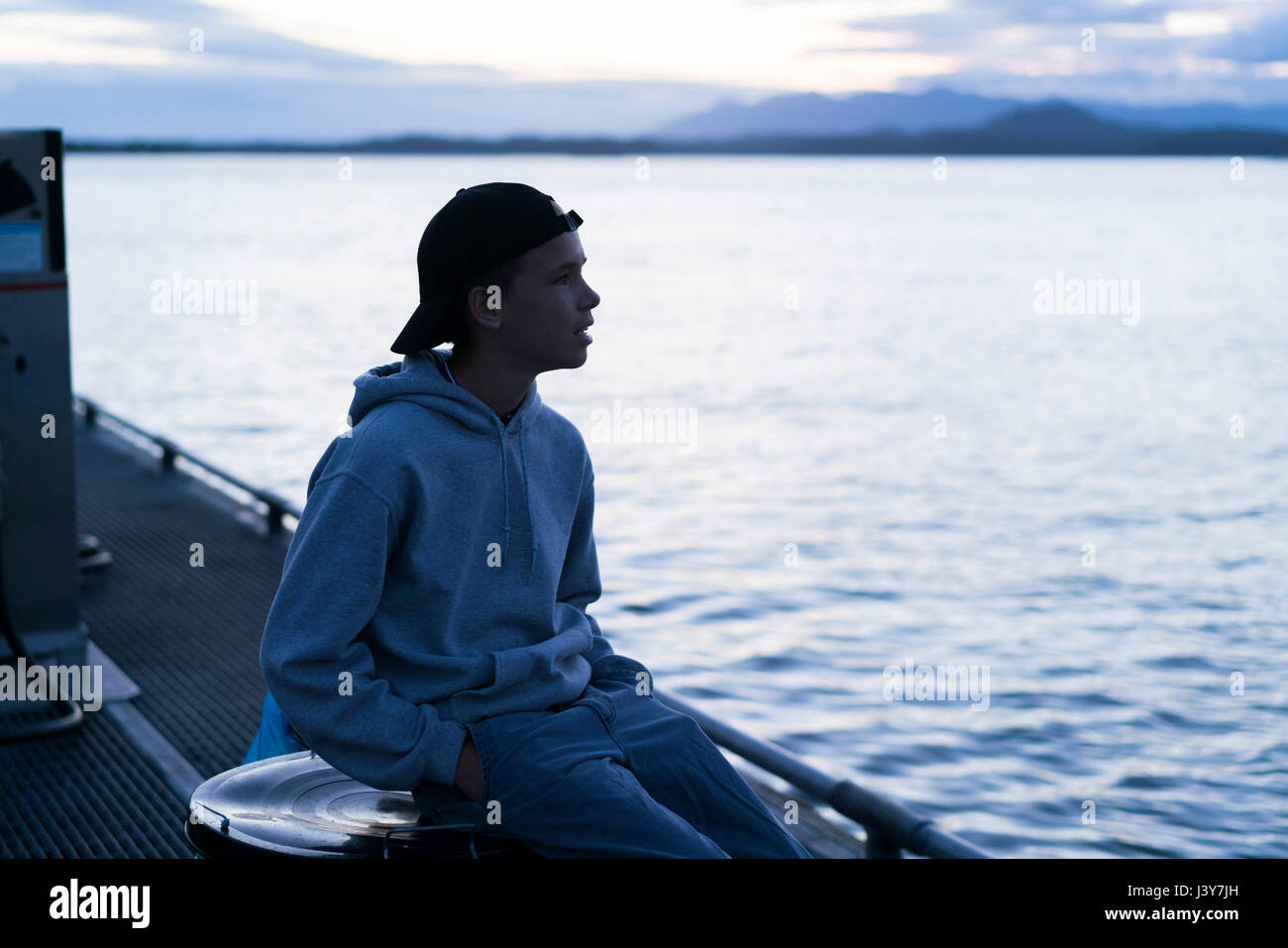 Teenage boy sitting on dock looking away, Pacific Rim National Park, Vancouver Island, Canada Stock Photo