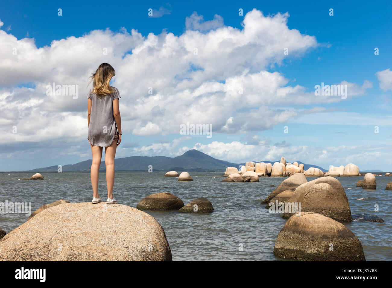 Rear view of teenage girl on rock looking at view of sea Stock Photo ...