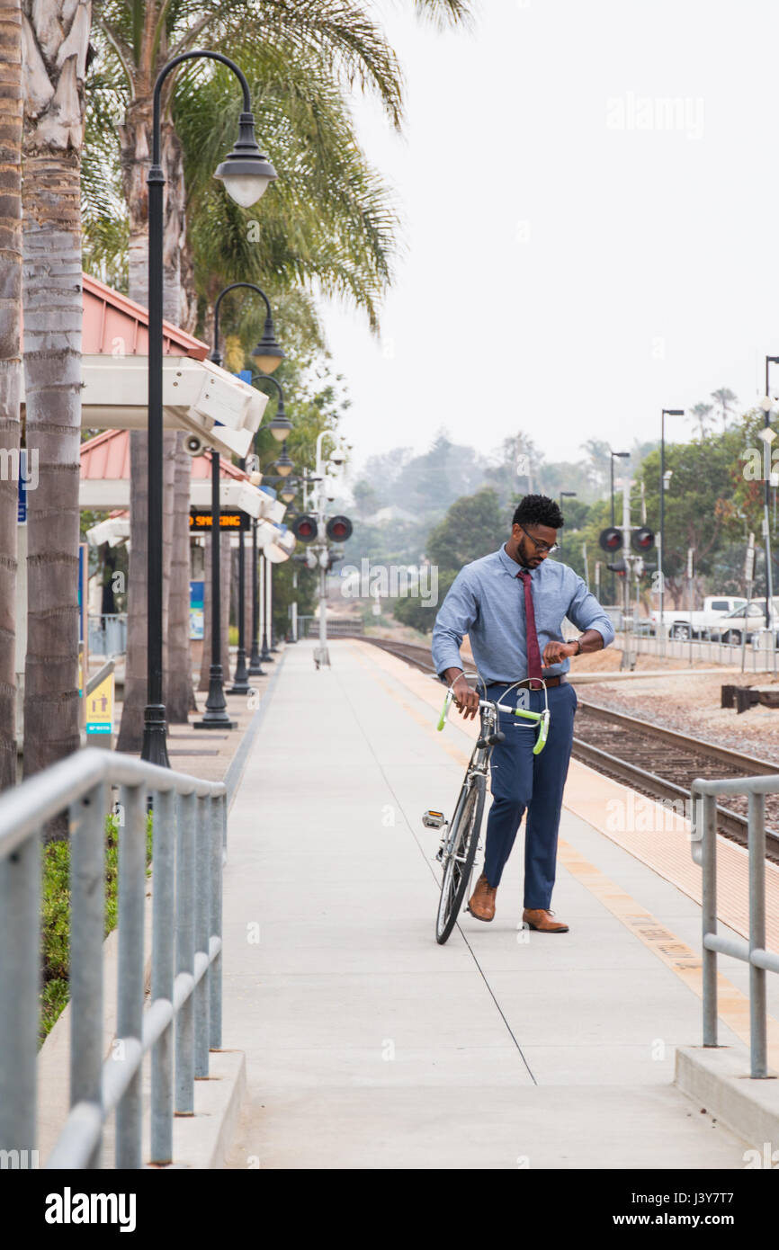 Young businessman cyclist looking at watch on railway station platform Stock Photo