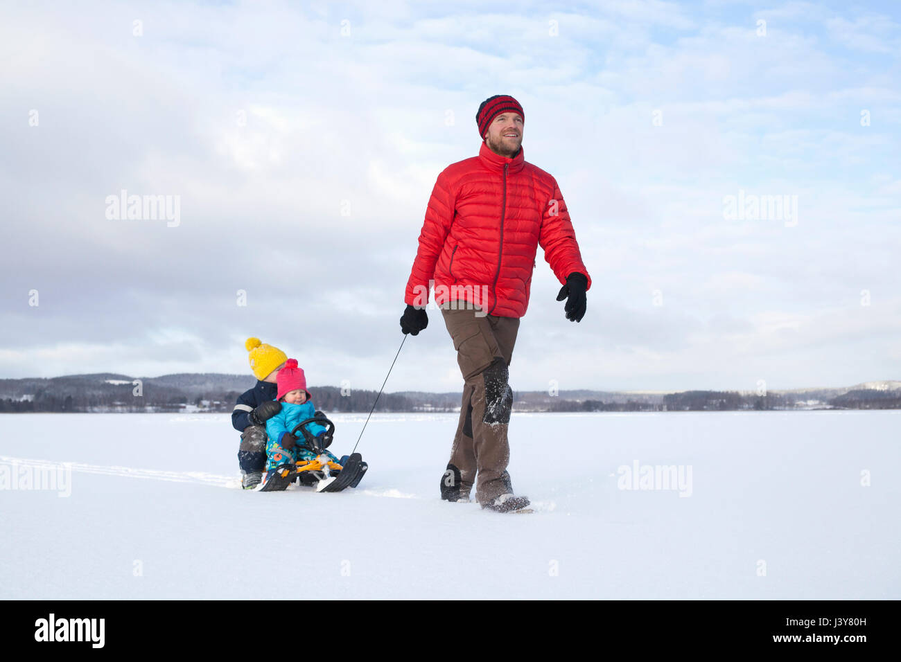 Father pulling sons along on sledge in snow covered landscape Stock