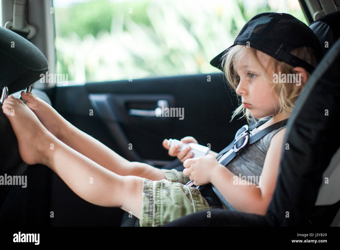 Young boy sitting in child's seat in back seat of car, bored expression Stock Photo