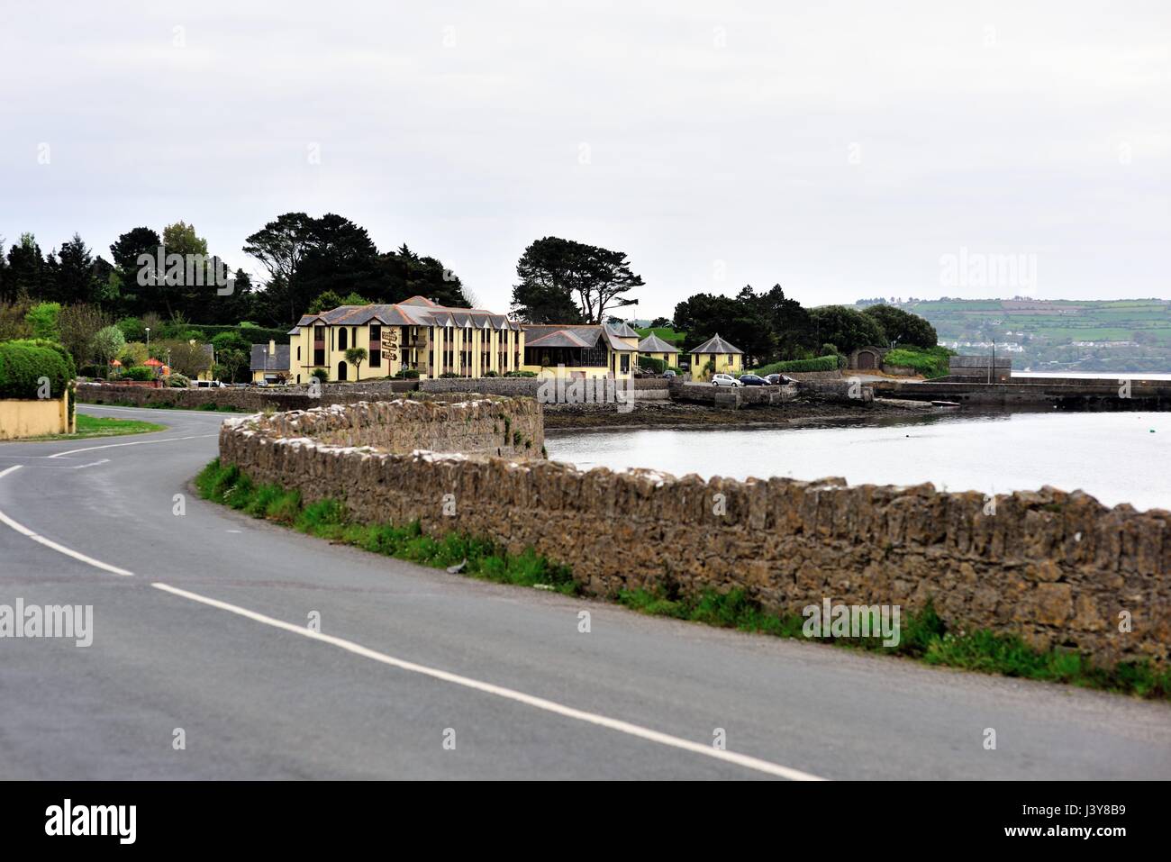 A winding roadway and wall follow the contours of the harbor leading to a resort in the Irish coastal community of Dungarvan in County Waterford. Stock Photo