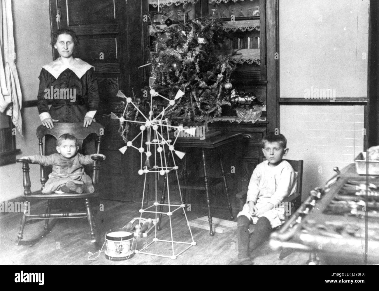 A woman and [probably] her sons, with a small table Christmas tree, c.1916.  They pose in the kitchen of an above-average home. I think the woman is a servant in the house, and this is her family's Christmas celebration.  To see my other Christmas-related vintage images, Search:  Prestor  vintage  holiday Stock Photo