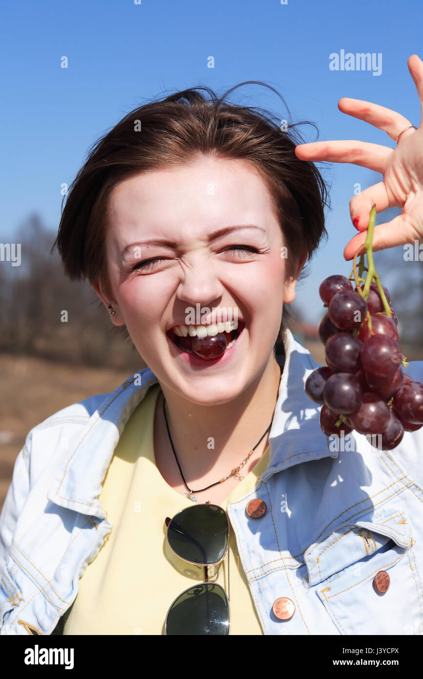 Beautiful young girl eating red grapes outdoor on blue sky background