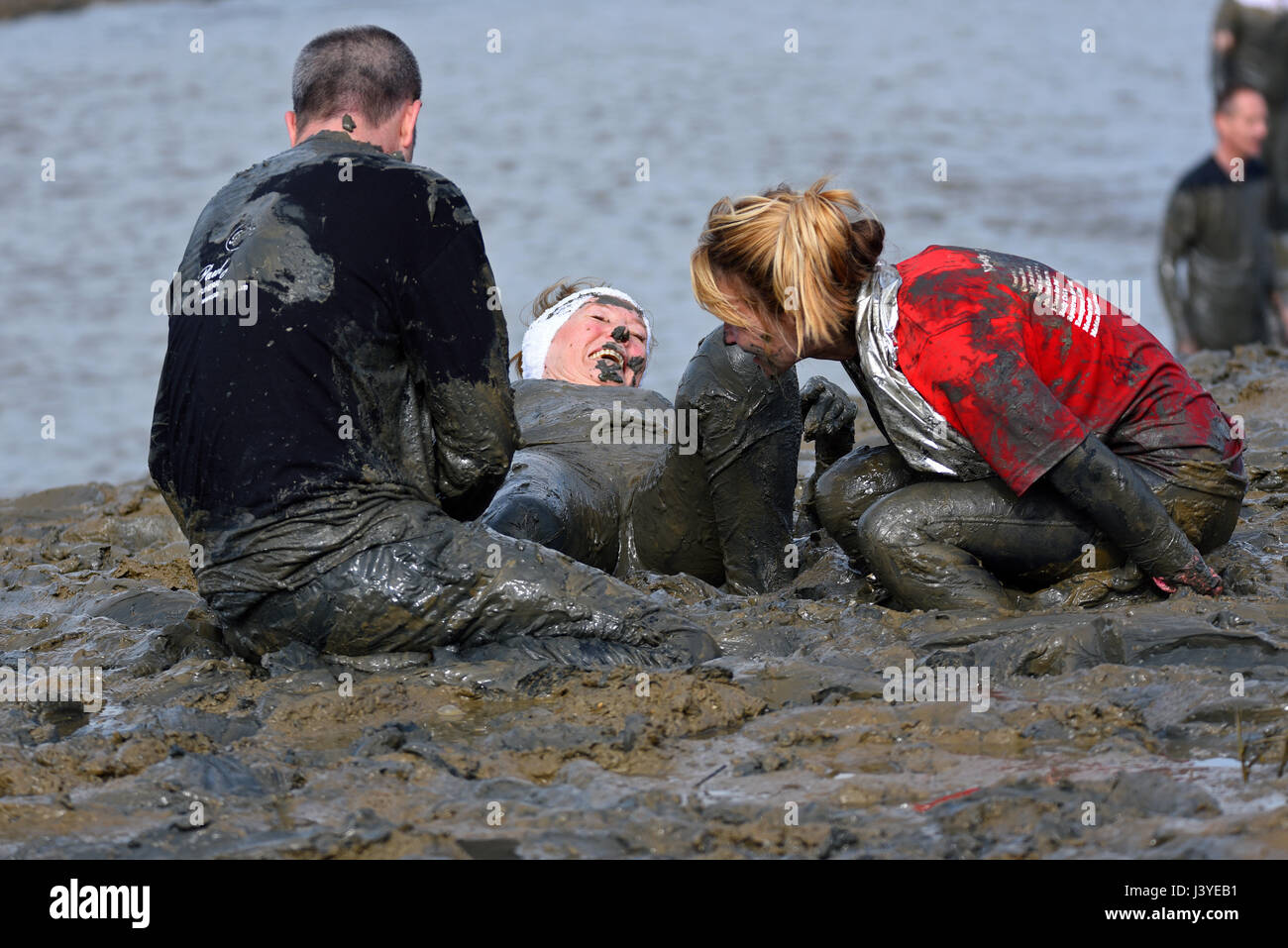 Mad Maldon Mud Race competitors covered in mud from racing through and across the River Blackwater in Essex, UK Stock Photo