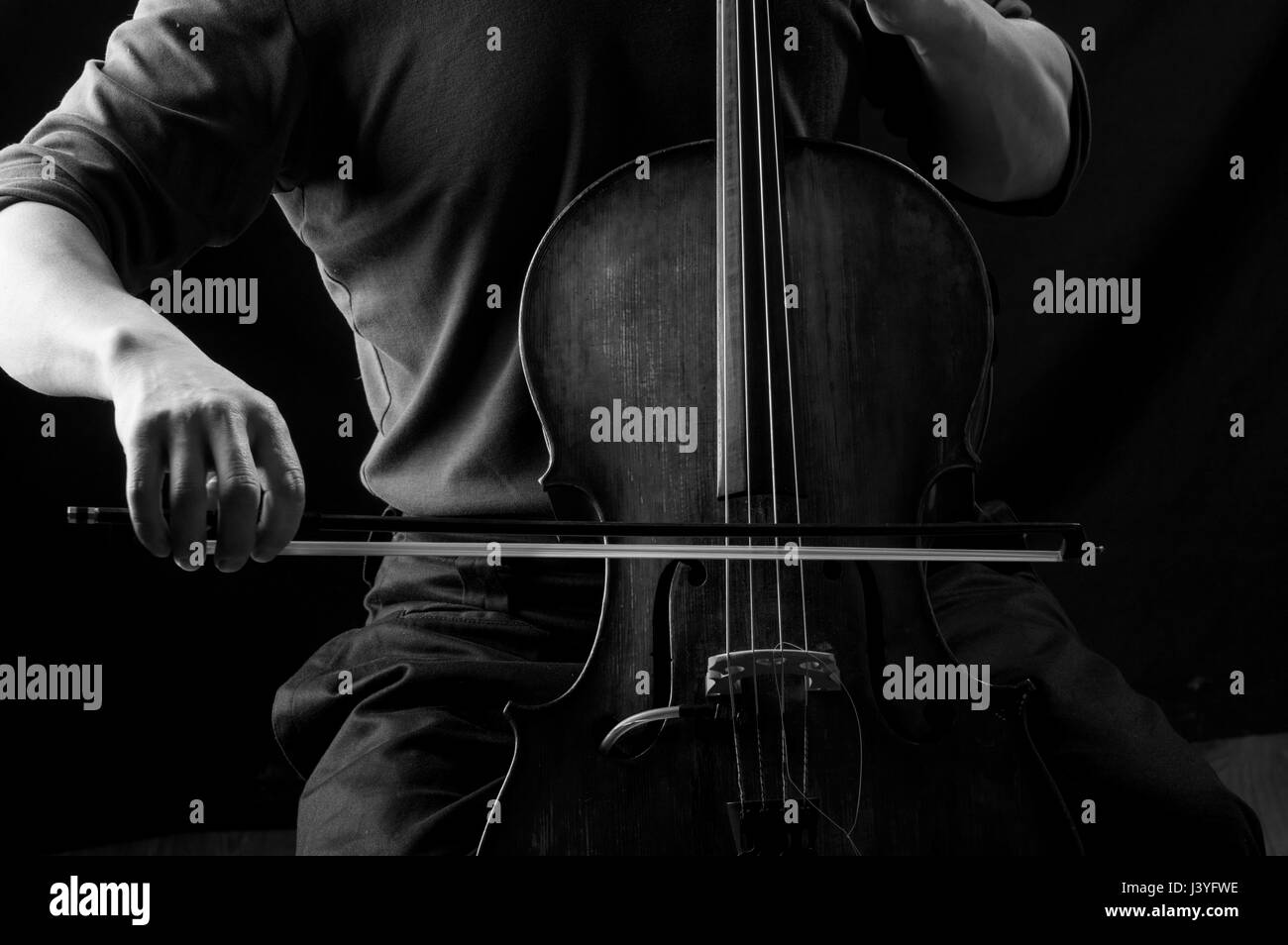 Black and white photograph of a man in playing cello with a bow, his face hidden Stock Photo