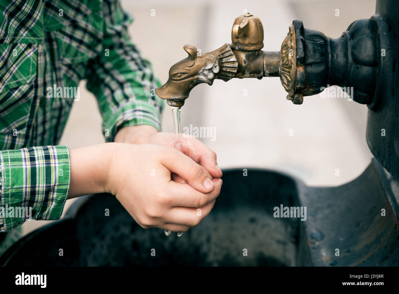 A teen boy washing his hand in public water fountain Stock Photo