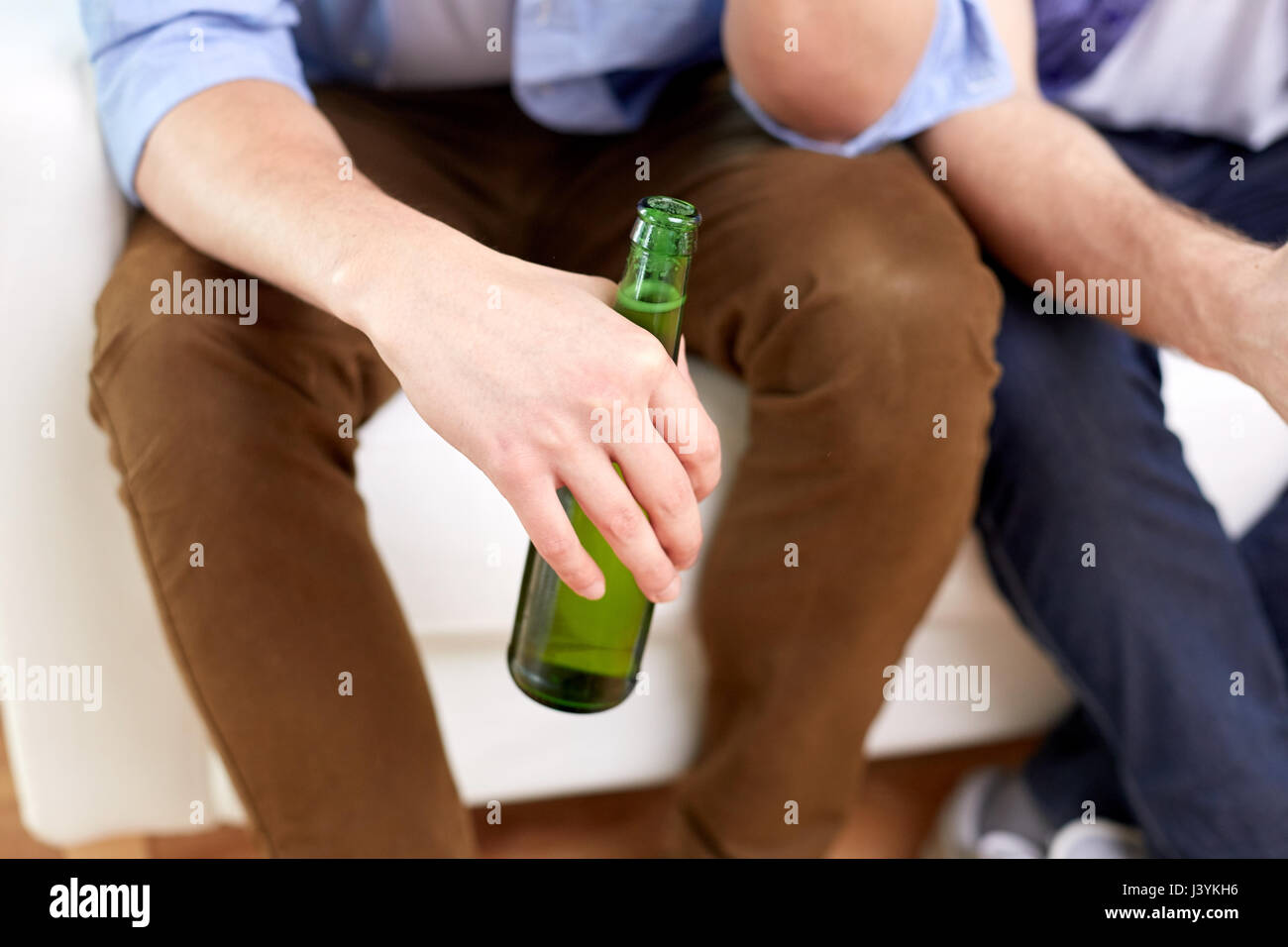men with beer bottles sitting on sofa at home Stock Photo