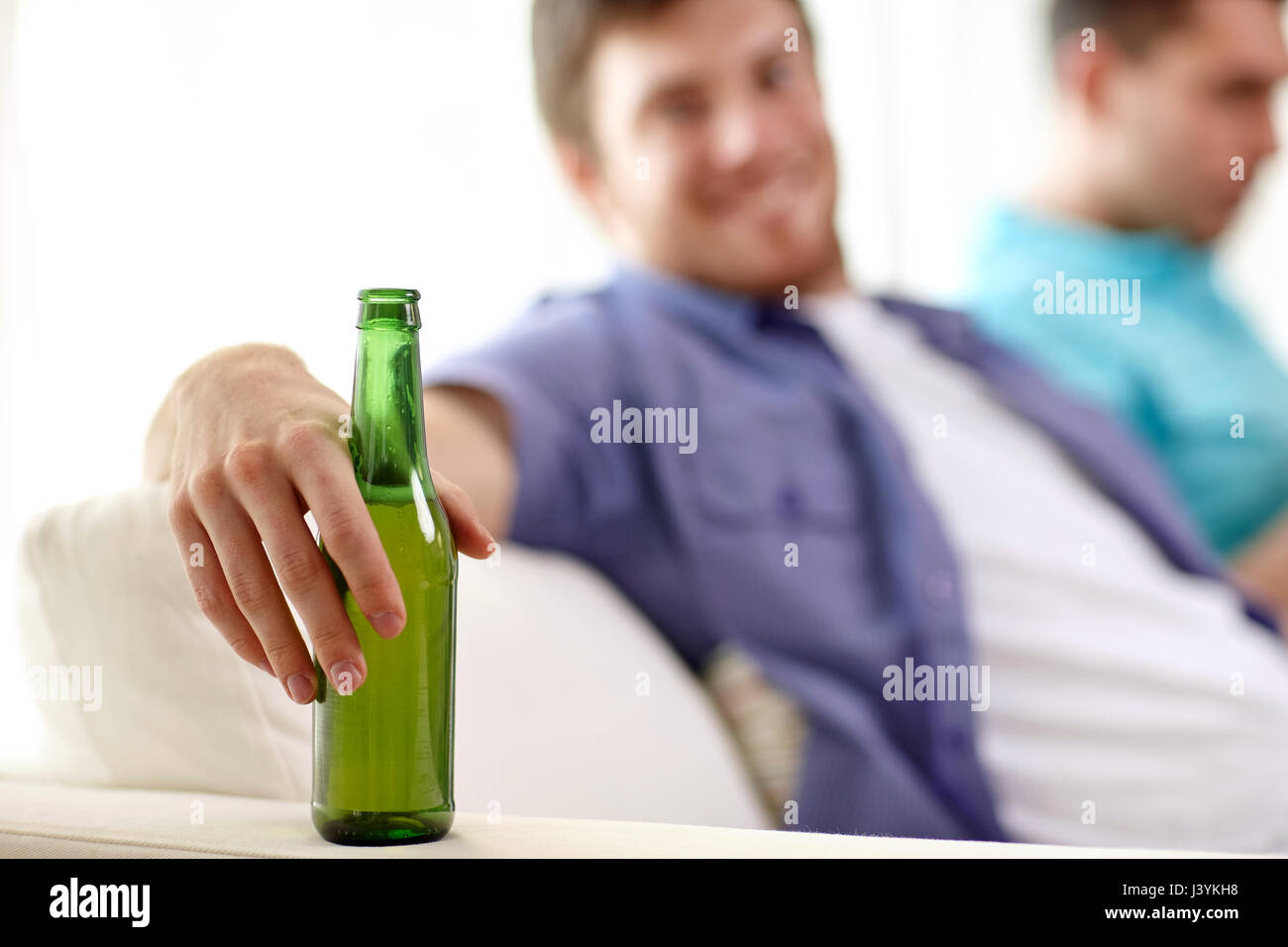 men with beer bottles sitting on sofa at home Stock Photo
