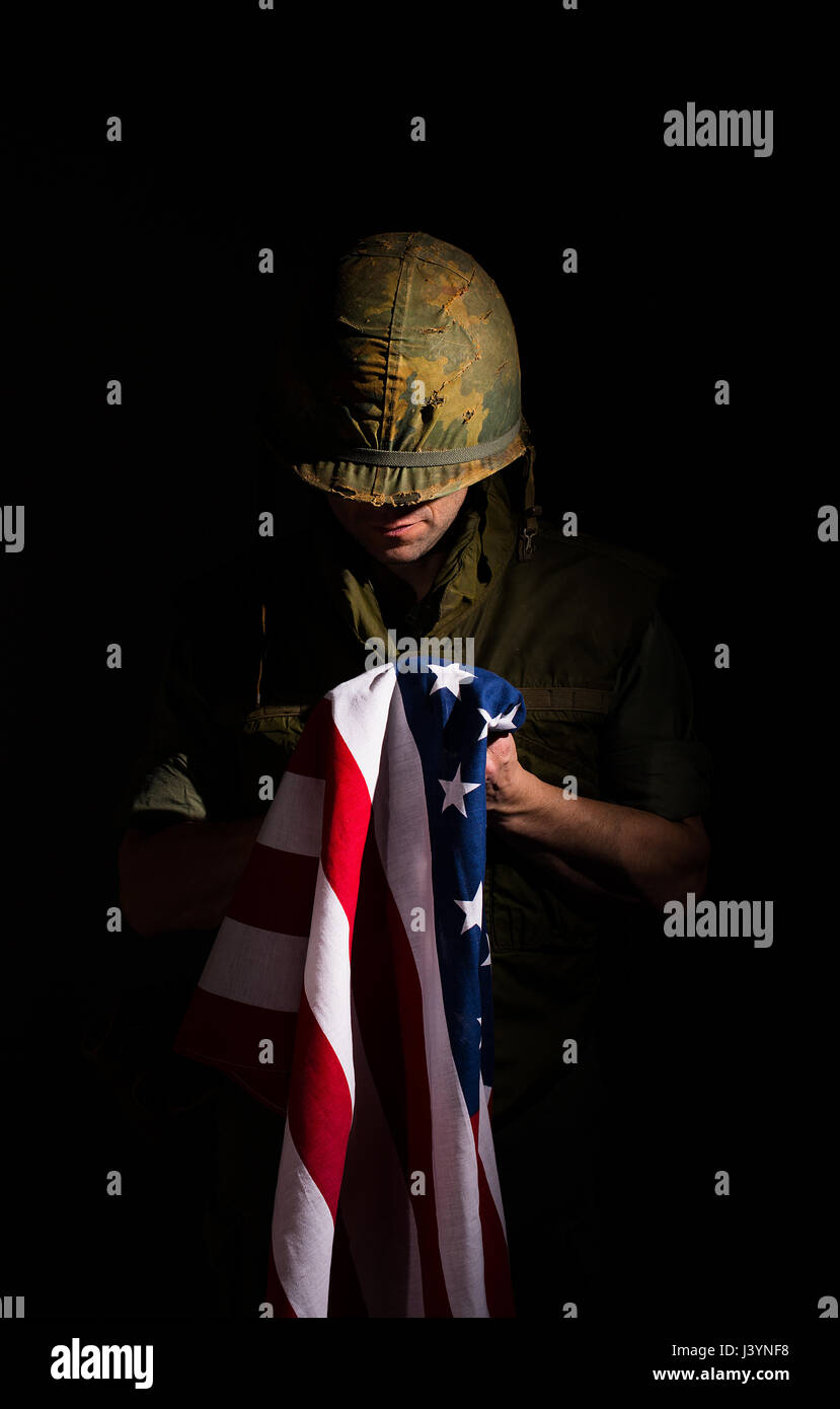 US marine from the Vietnam War holding the American flag against a dark black background. Stock Photo