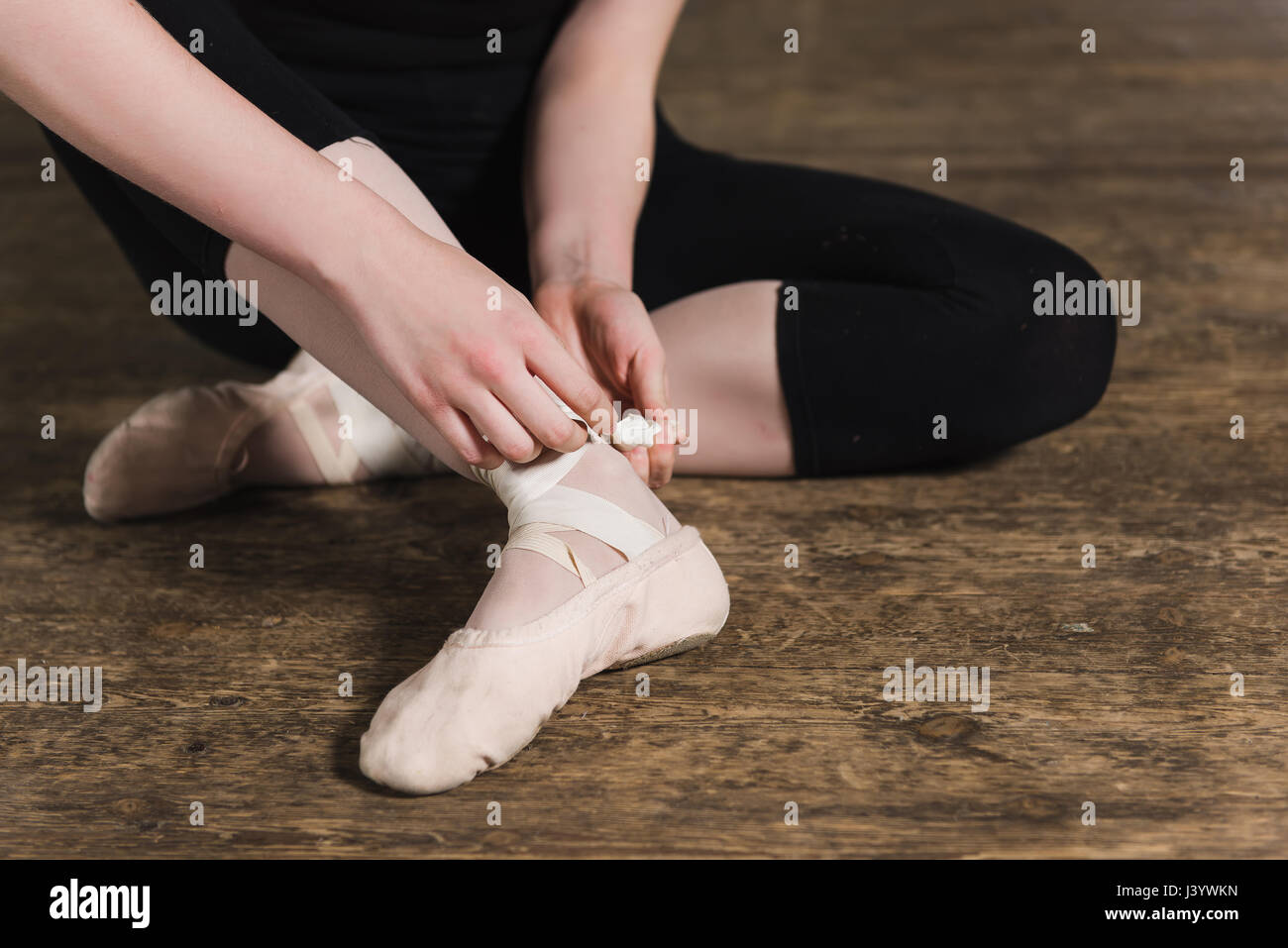 Female dancer ties on her pink ballet slippers with ribbons Stock Photo