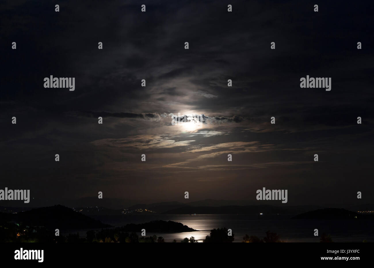 Long exposure of full moon in 2016 summer behind clouds over Aegean sea at Turkbuku village in Bodrum peninsula. Light shines on sea surface. Stock Photo