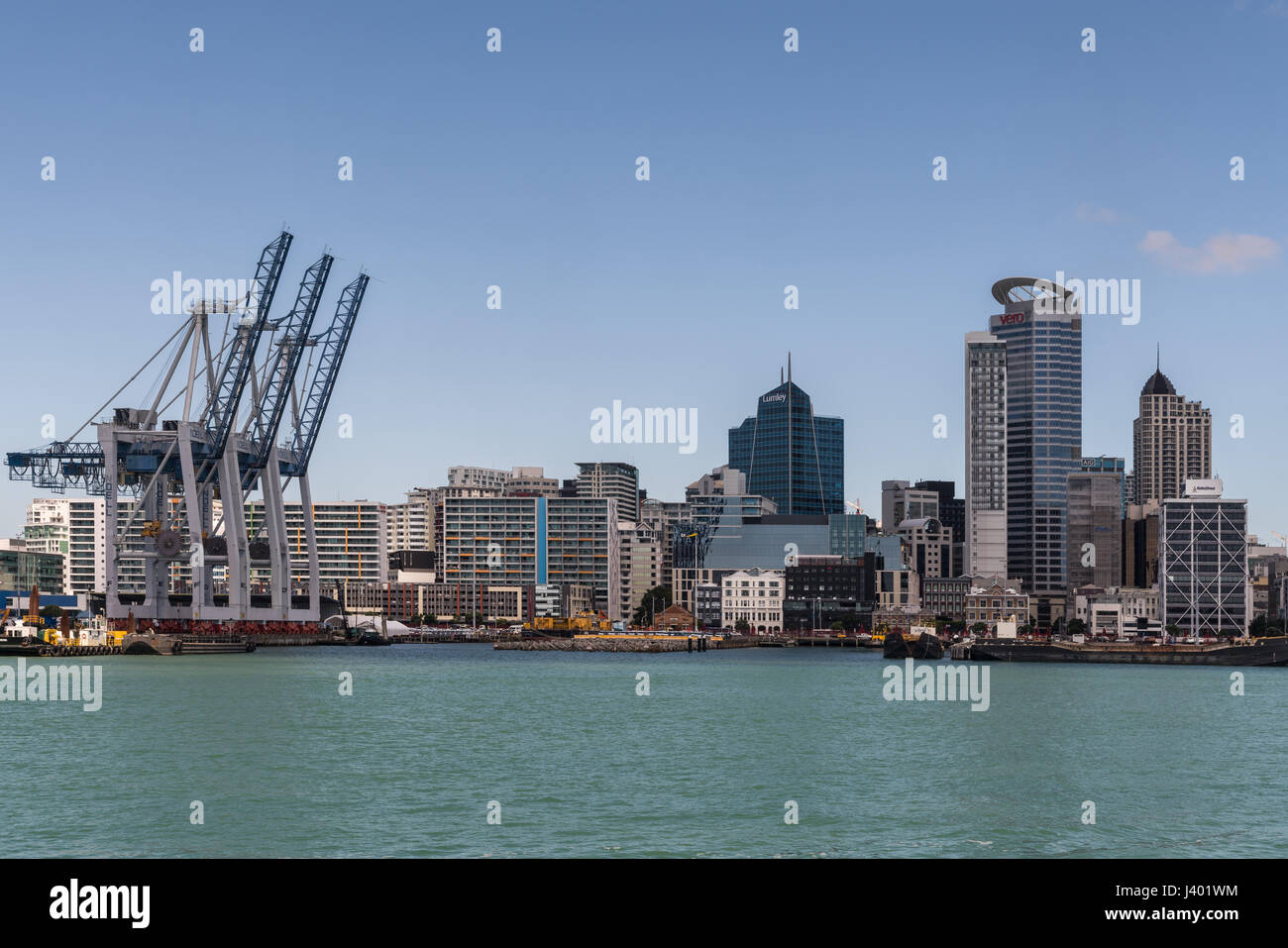 Auckland, New Zealand - March 3, 2017: Row of container cranes at Commercial Harbor with part of city skyline in back under blue sky and behind greeni Stock Photo