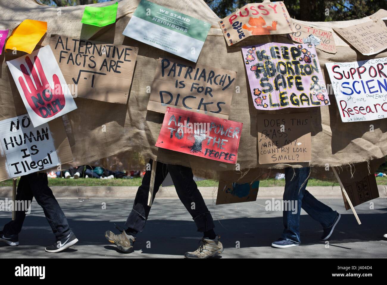 People march in a costume covered with protest signs at the Mayday