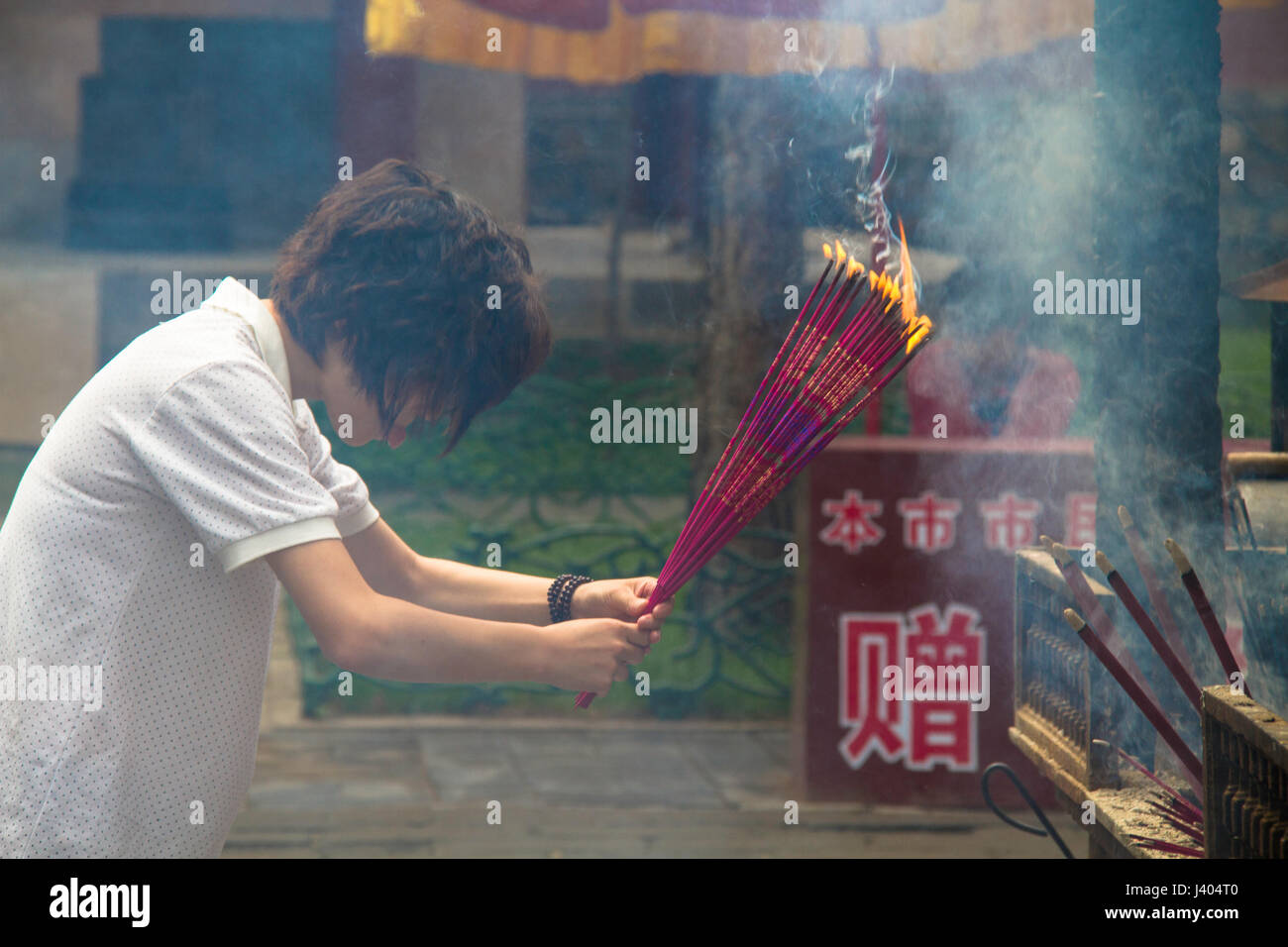 A young Chinese woman bows while holding burning incense at a Tibetan Buddhist temple in Chengde, China Stock Photo