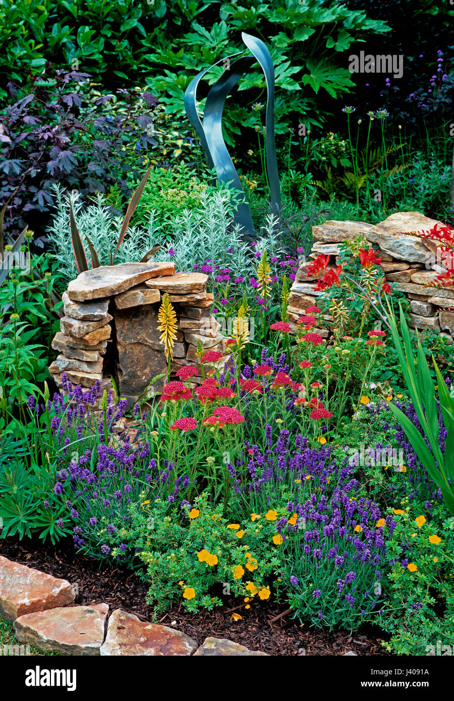 Colourful garden corner with dry stone wall and colourful plants Stock Photo