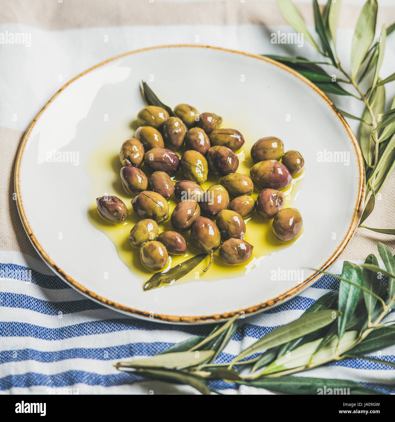 Pickled green Mediterranean olives and olive tree branch on towel Stock