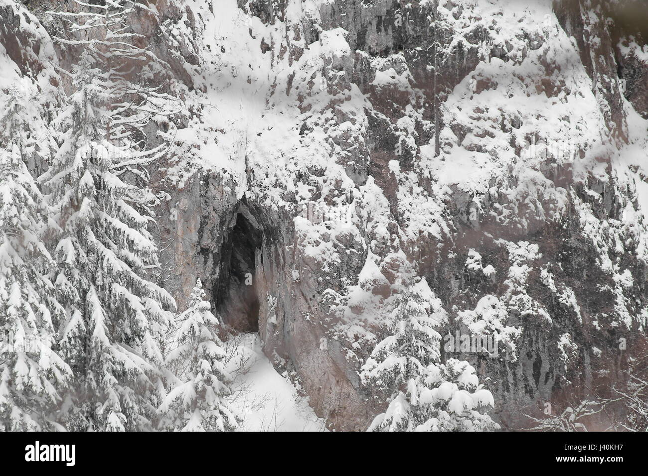 Cave in a snowy alpine rock cliff. Stock Photo