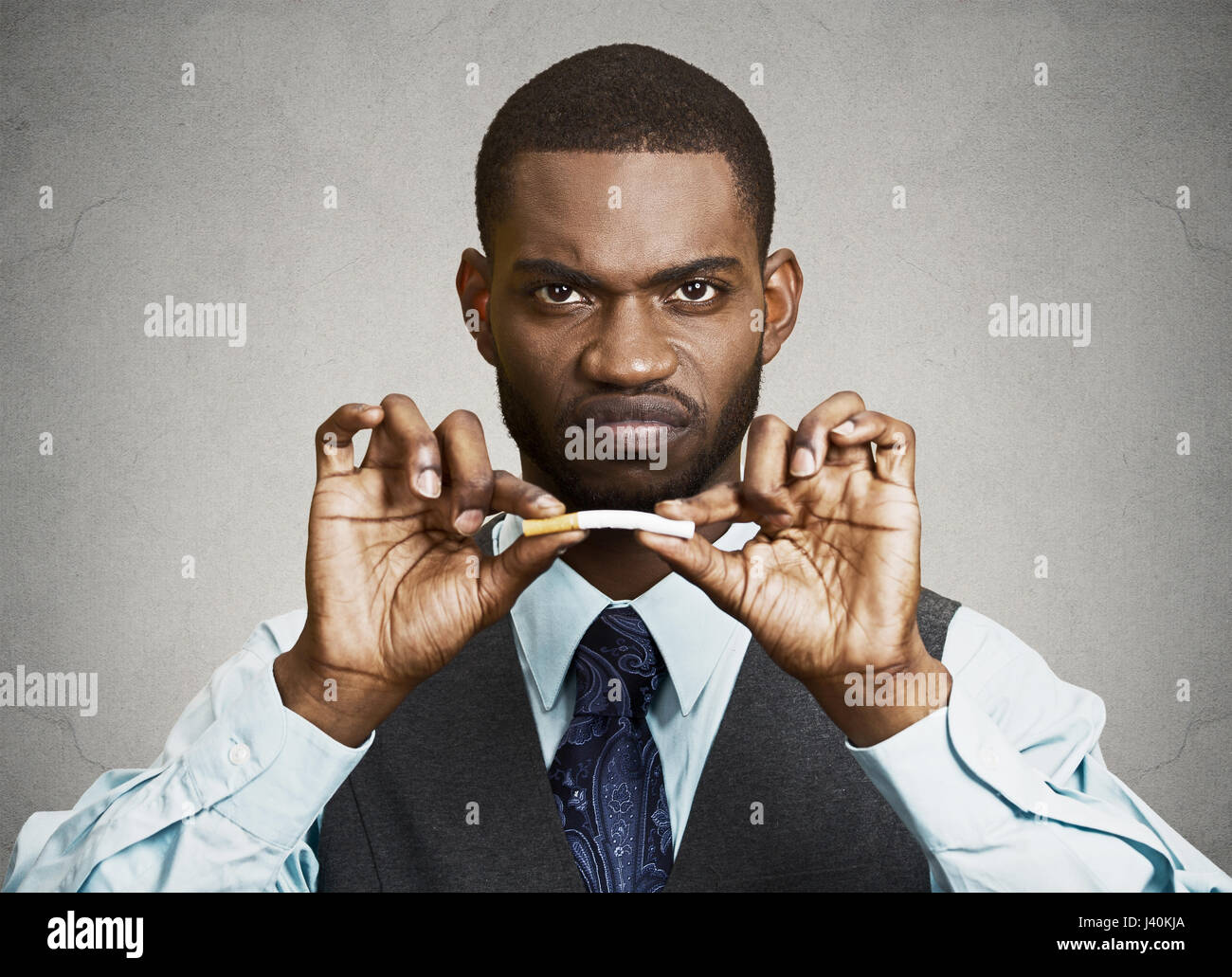 Closeup portrait, headshot, young, handsome, unhappy, angry  business man, corporate executive breaking cigarette, isolated black grey background. Lif Stock Photo