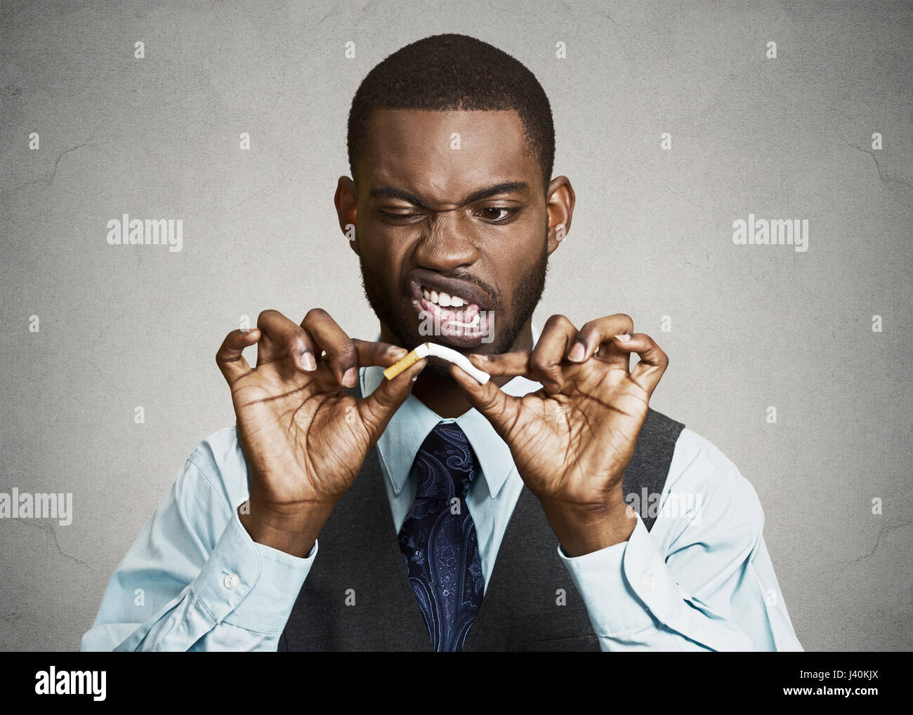 Closeup portrait, headshot, young, handsome, unhappy, angry  business man, corporate executive breaking cigarette, isolated black grey background. Lif Stock Photo