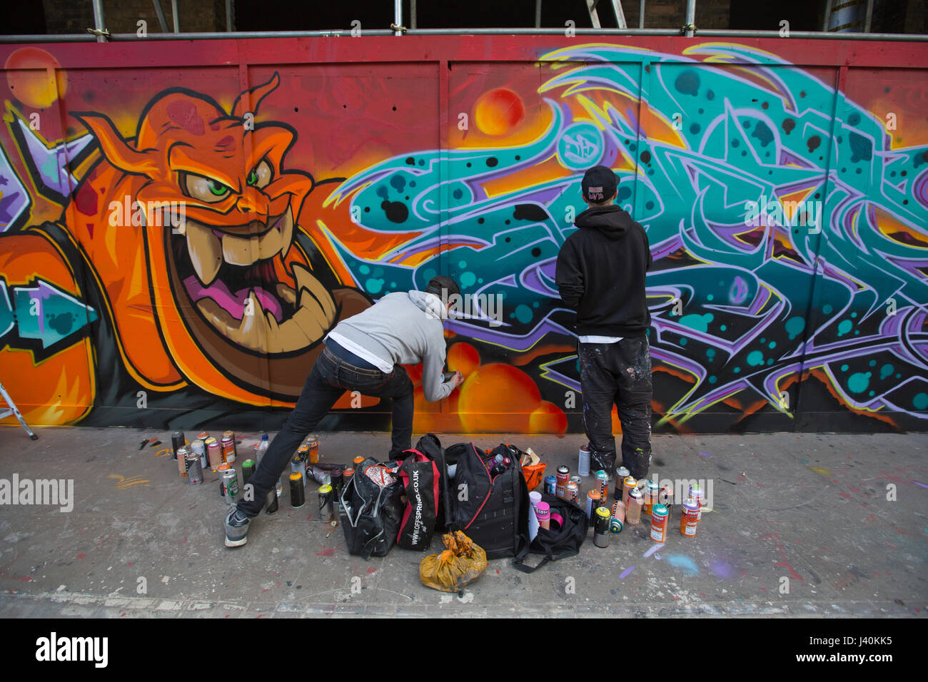 Street artist spray painting graffiti mural on hoarding along Great Eastern Street, Shoreditch