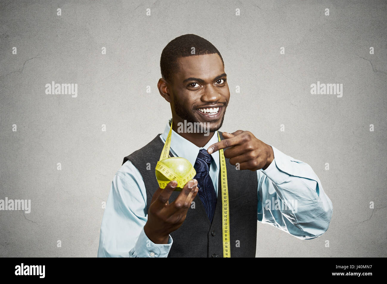Closeup portrait headshot business man, corporate executive holding, pointing at green apple measuring tape on neck isolated black grey background. He Stock Photo