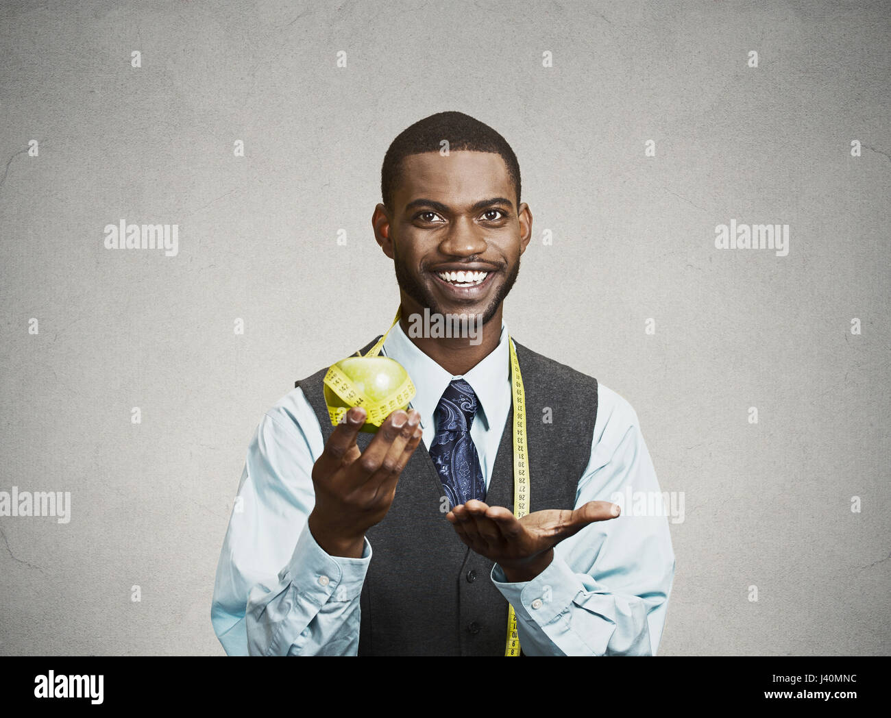 Closeup portrait, headshot business man, corporate executive holding, offering green apple, measuring tape on neck isolated black grey background. Hea Stock Photo