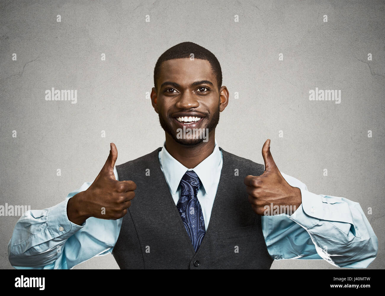 Closeup portrait handsome young smiling business man, corporate employee giving thumbs up sign at camera isolated black grey background. Positive huma Stock Photo