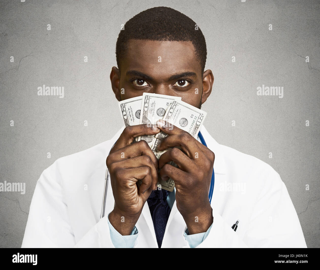 Closeup portrait grumpy greedy miserly health care professional, male doctor holding, protecting his money dollars in hand, isolated black background. Stock Photo