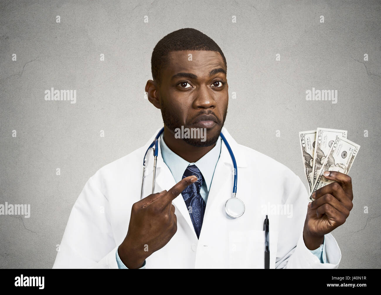 Closeup portrait grumpy greedy miserly health care professional, male doctor holding, pointing at his money dollars in hand isolated black background. Stock Photo