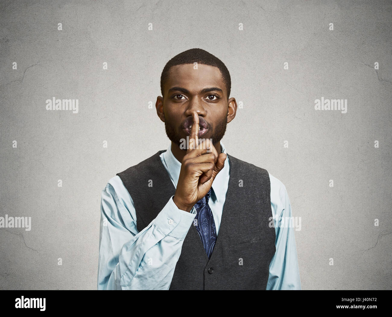 Closeup portrait young serious businessman placing finger on lips saying, shhh, be quiet, silence, isolated grey background. Facial expression, human  Stock Photo