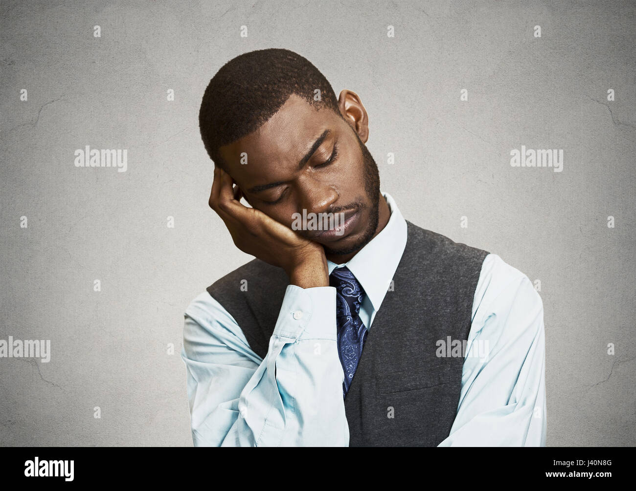 Closeup Portrait Sleepy young Business Man, funny guy placing head on hand, unhappy, Eyes Closed,  isolated grey wall background. Negative human emoti Stock Photo