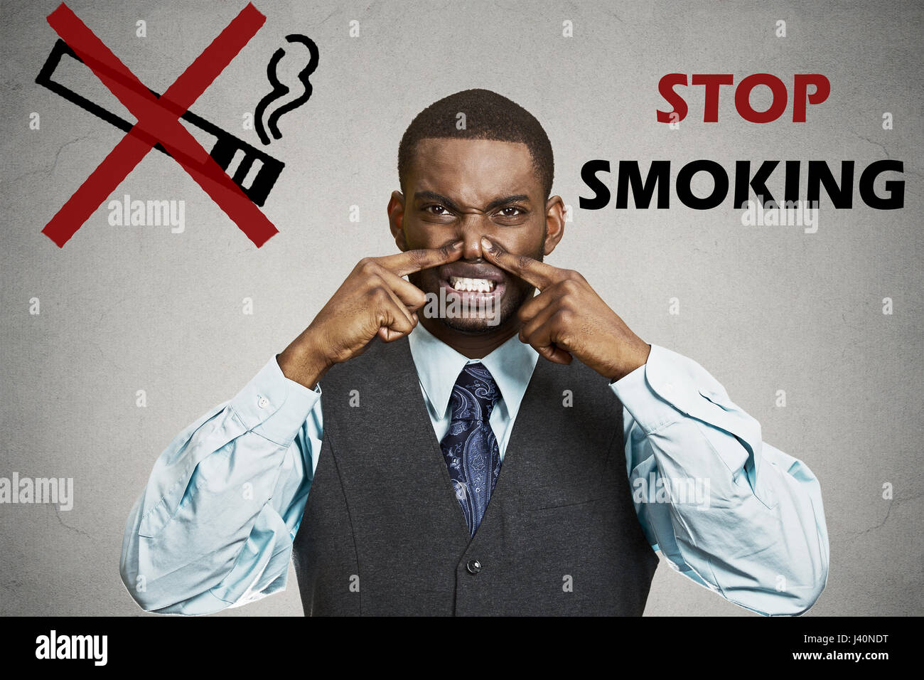 Portrait young man, pinches his nose, something stinks bad smoke smell, grey wall background, stop smoking sign. Negative face expression, body langua Stock Photo