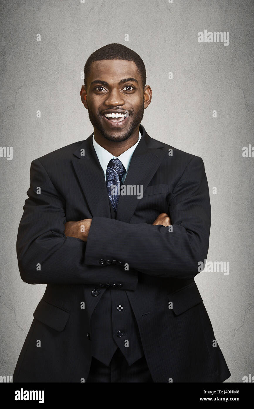 Confidence and charisma. Closeup portrait Cheerful young African man in full suit keeping arms crossed, looking at camera, isolated grey wall backgrou Stock Photo