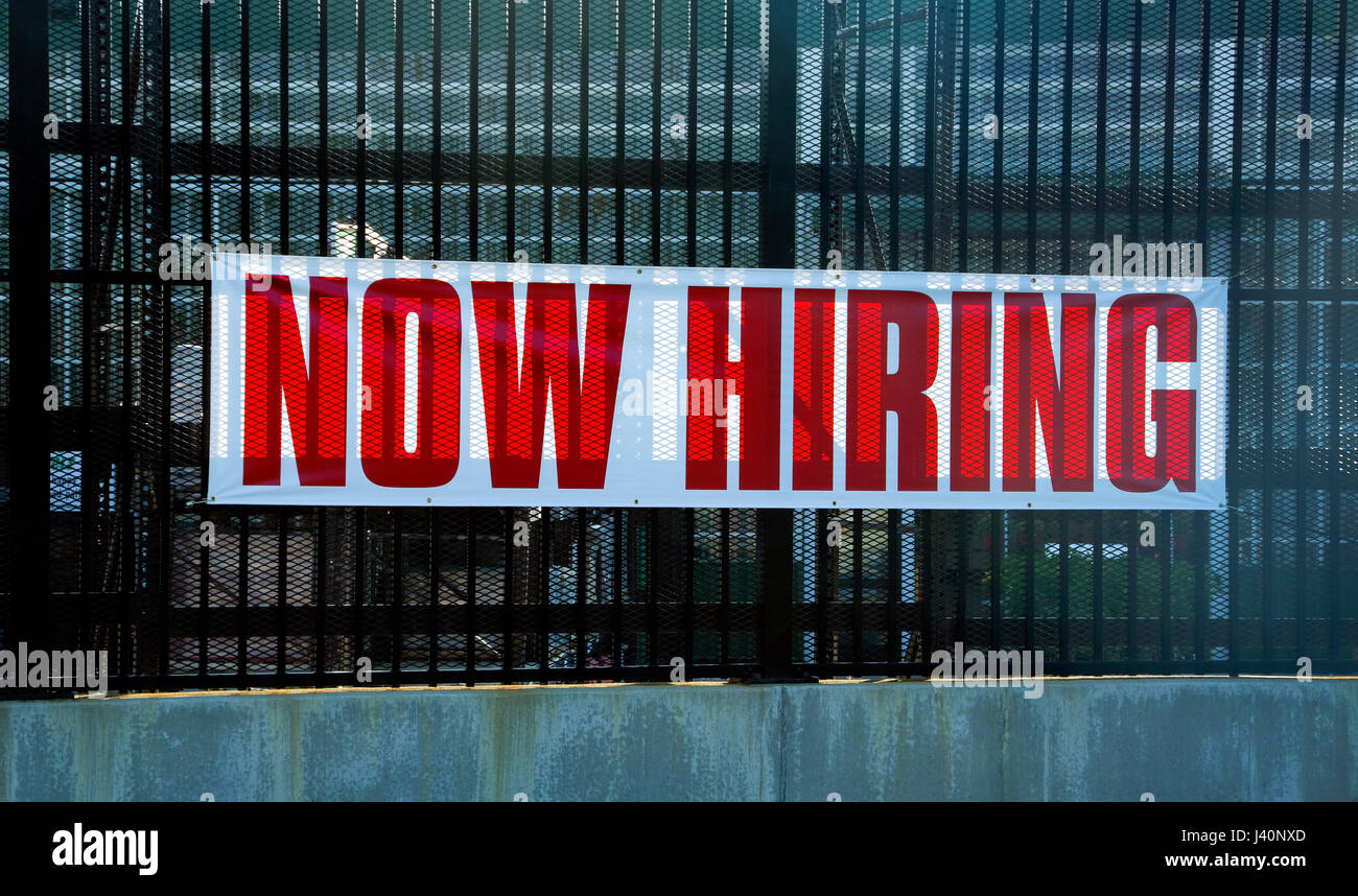Now Hiring, help wanted sign on industrial fence Stock Photo