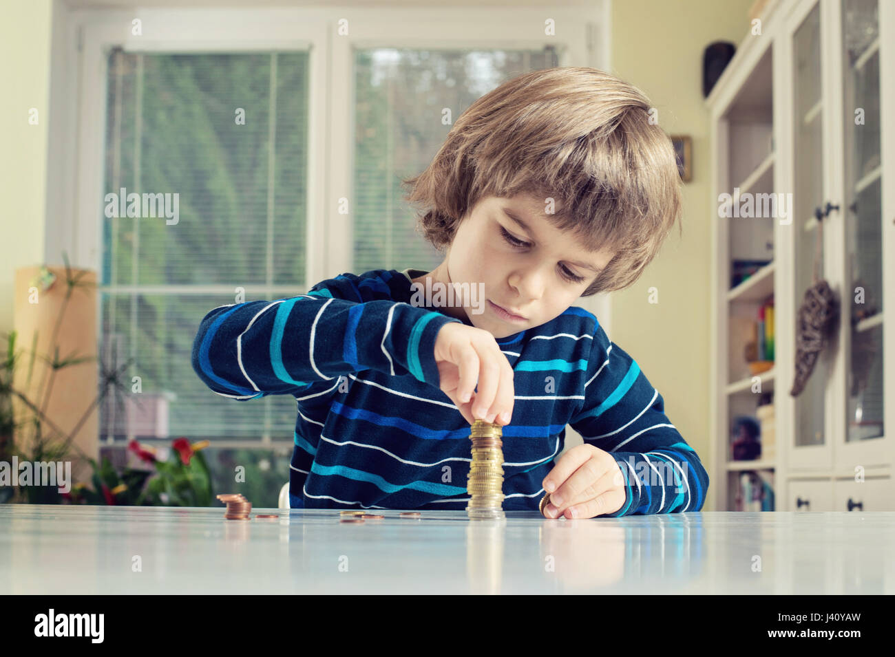 Little boy making stack of coins, counting money at table. Learning financial responsibility and planning savings concept. Stock Photo