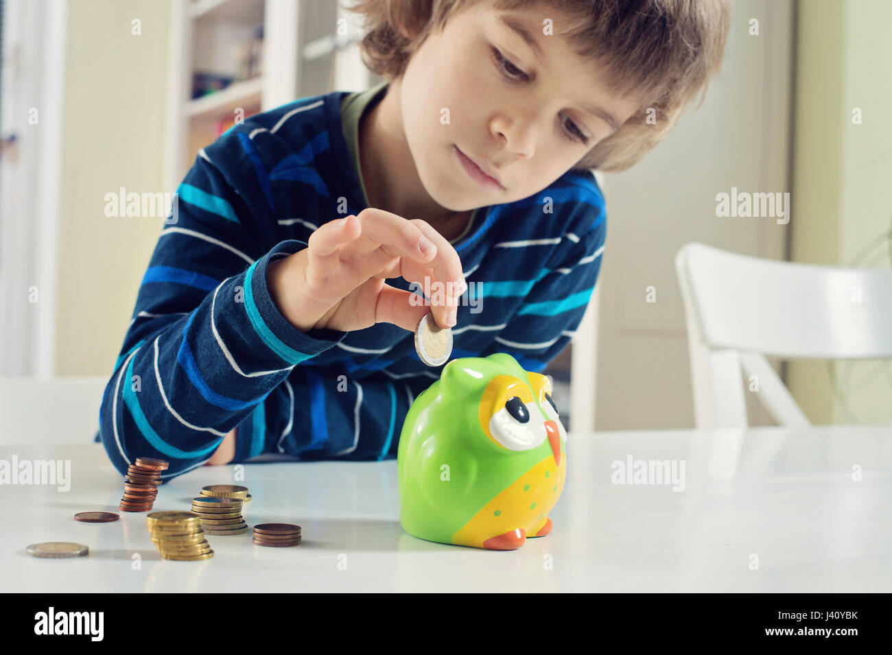 Little boy putting coins into owl piggy bank. Learning financial responsibility and projecting savings. Stock Photo