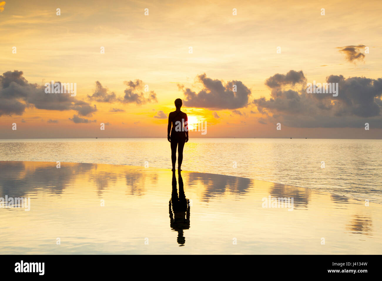 Figure silhouetted at sunset over an infinity pool Stock Photo
