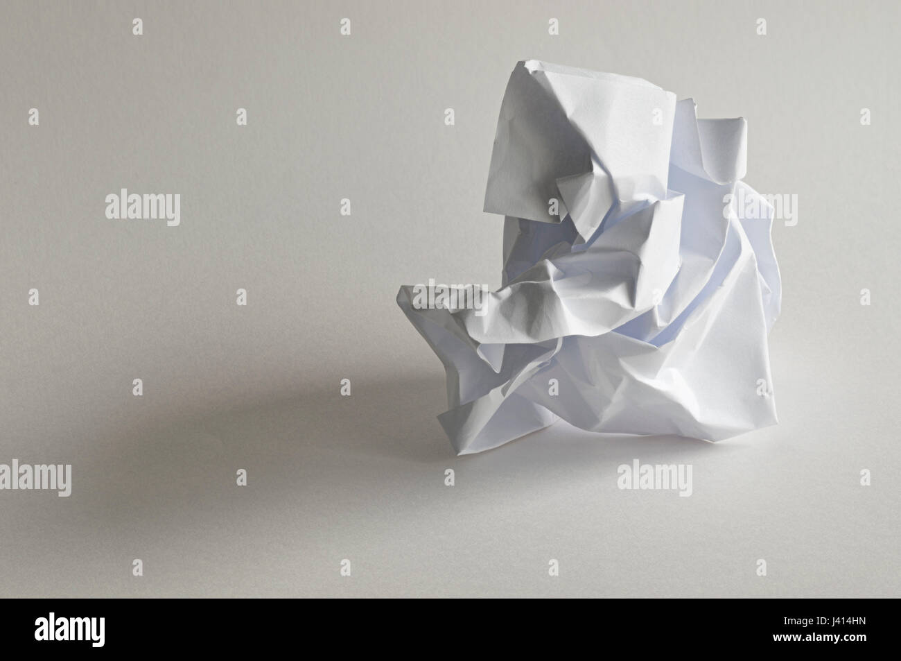 Focus-stacked study of crumpled ball of paper resembling meditating monk, natural light, white paper background with subtle colours in shadows. Stock Photo