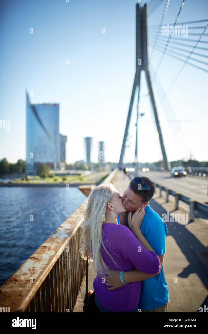 Couple on Vansu Tilts bridge, Svedbank office building The Sun Stone in the background, Daugava river, view towards Kipsala, Riga, Latvia Stock Photo